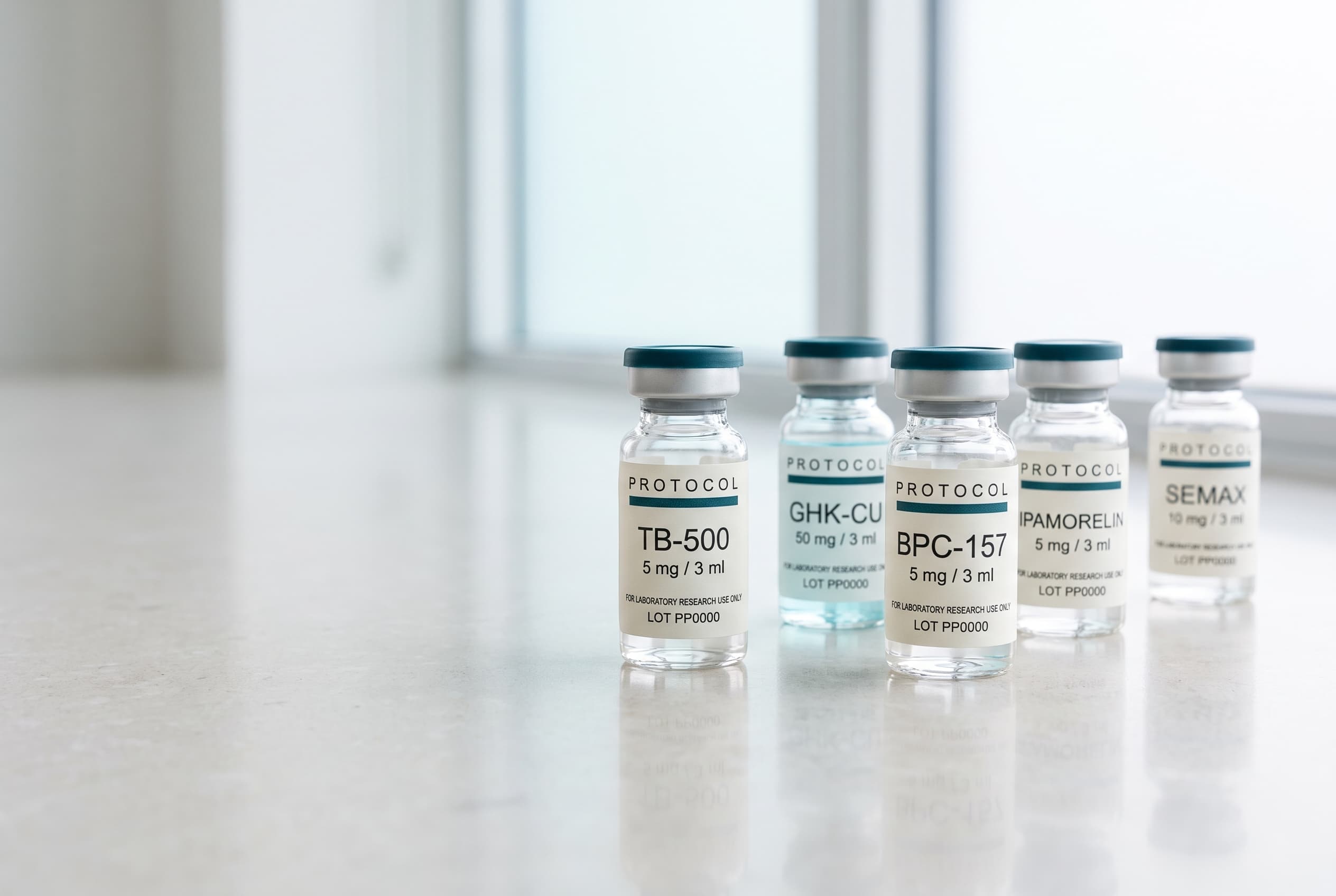 Five labelled Protocol Peptides vials in a row: TB-500, BPC-157, GHK-Cu in pale blue, Ipamorelin and Semax